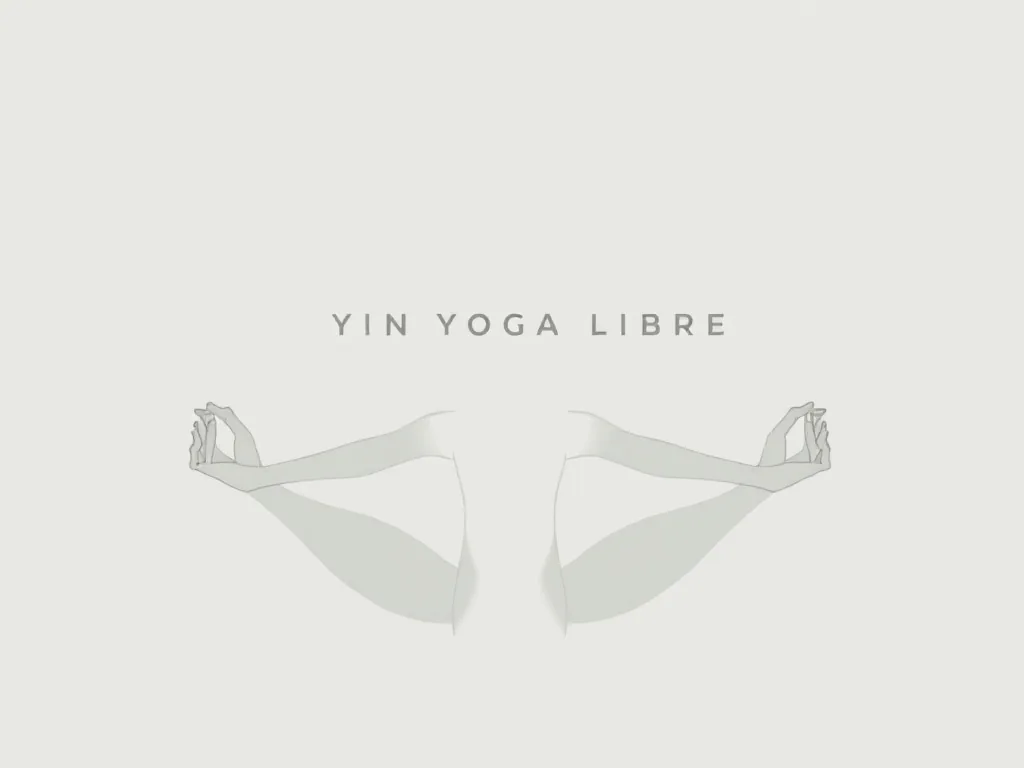 Un livre ouvert sur un tapis de yoga, une couverture pliée à côté, montrant des illustrations de postures de yin yoga avec